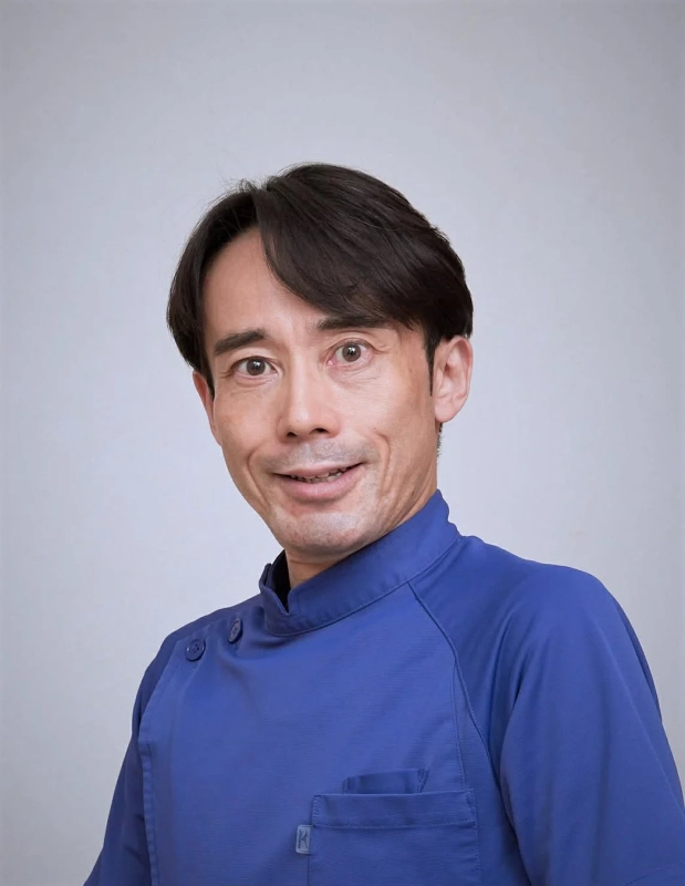 ブルーのユニフォームを着た中年のアジア人男性が、カメラに向かって優しく微笑んでいる