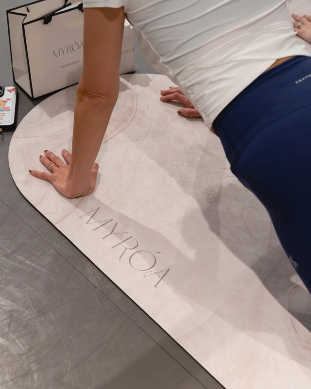 ヨガマットの上でエクササイズをする女性の姿。MYRÓAのロゴが入ったヨガマットとショッピングバッグ