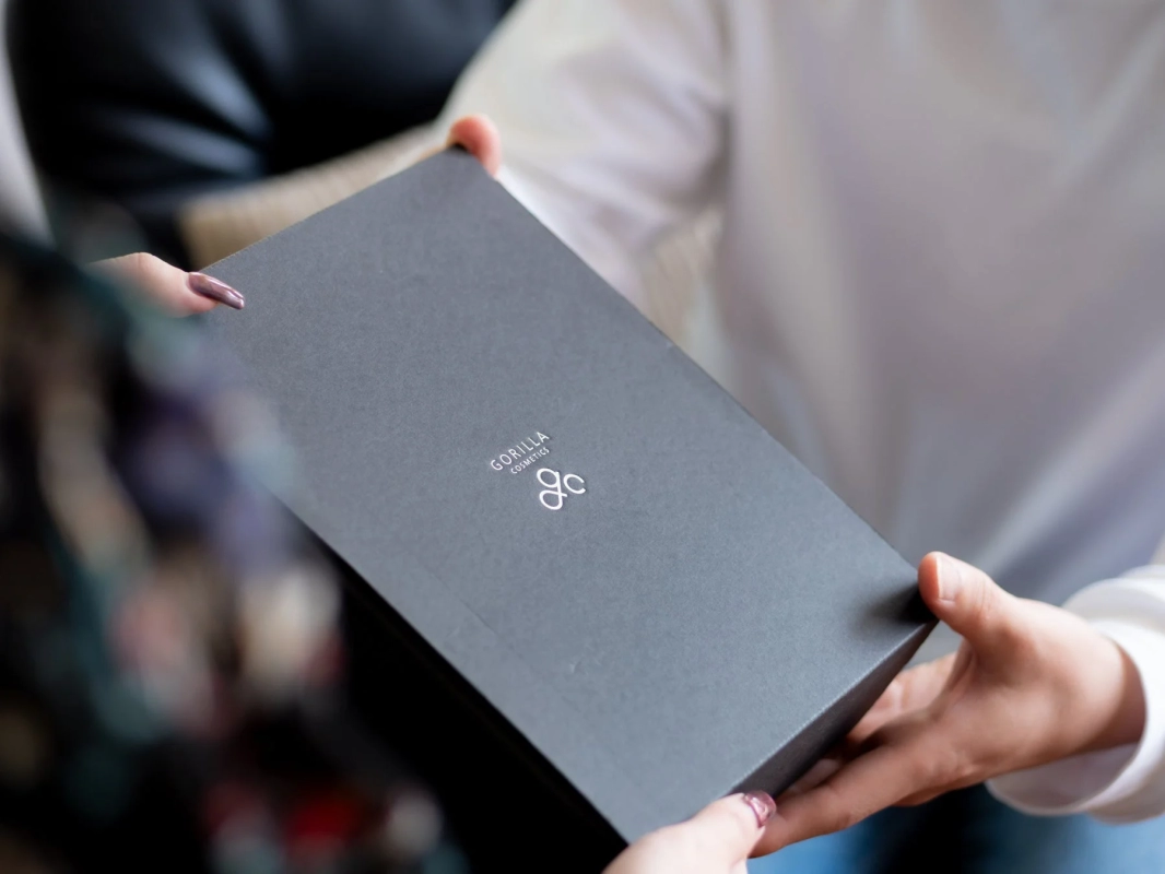 「GORILLA COSMETICS」と書かれた黒いギフトボックスを、二人の人物が手渡ししているクローズアップ写真です。