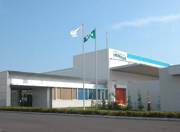 晴れた日に撮影された、近代的な外観の建物と企業フラッグが印象的な施設です。建物には「MARS COMETS FRONTIER」の看板があり、企業の事業所や工場であることが伺えます。手入れされた植栽と広い敷地が特徴です。