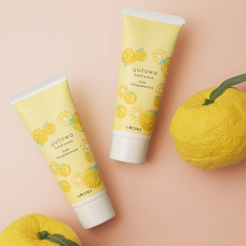 ピンク色の背景に、ゆずのイラストが描かれた「yutowaハンドクリーム」が2本と、実物のゆずが配置されています。北川村産のゆずを使用したハンドクリームであることが伝わる、明るく爽やかな商品画像です。
