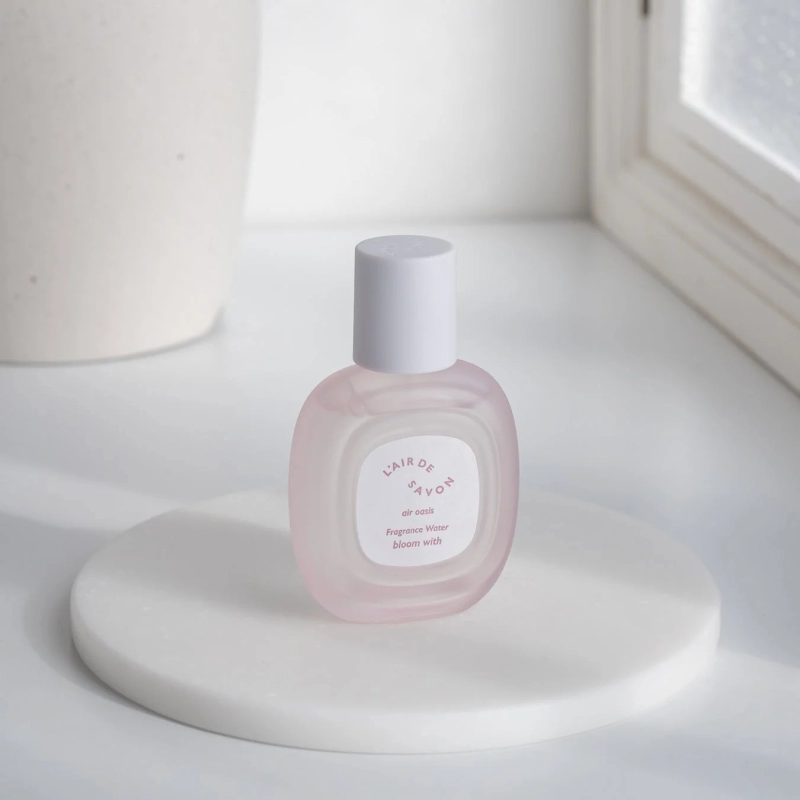 白い丸い台座の上に置かれた、ピンクがかった透明なフレグランスウォーターのボトル