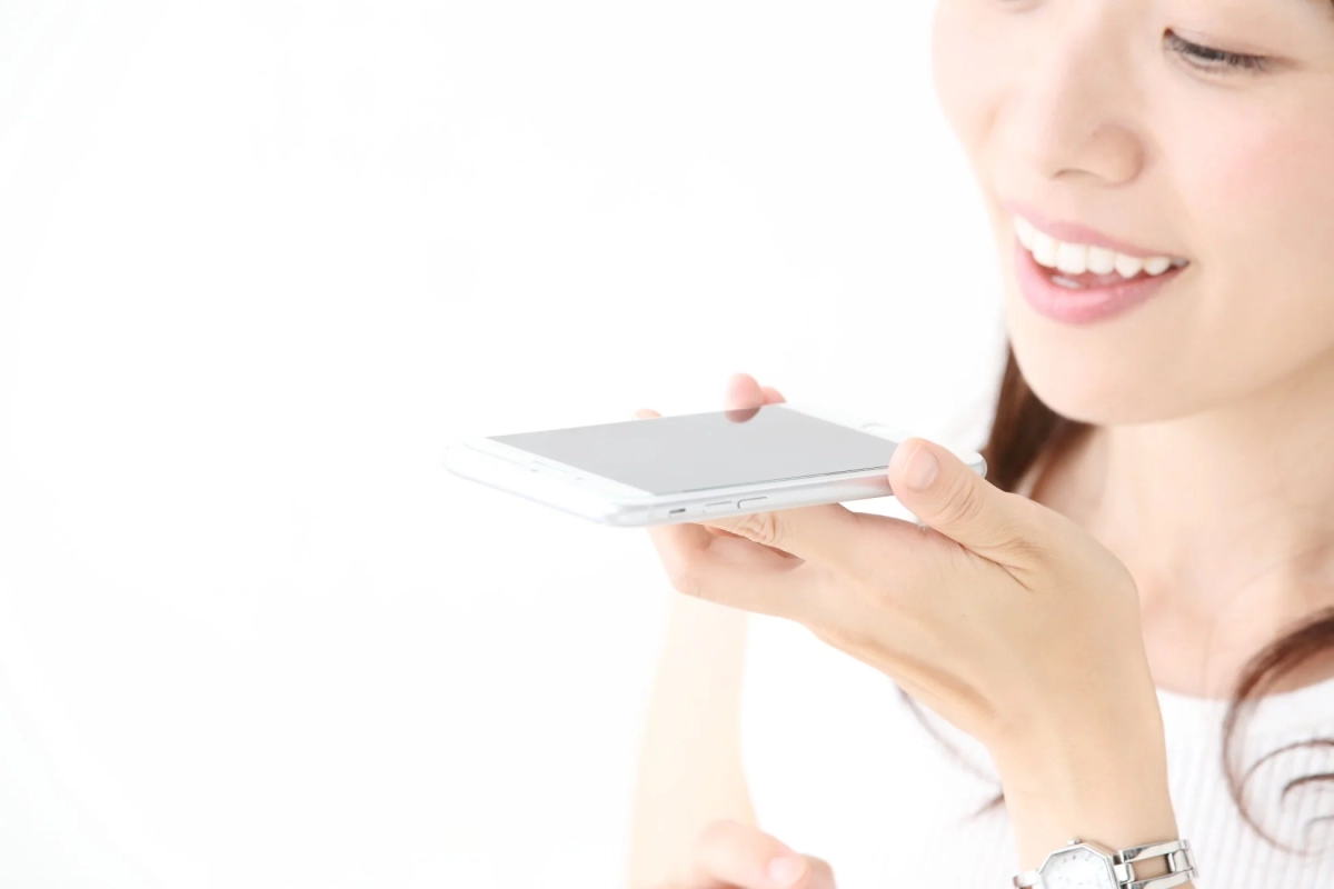 白い背景の前で、女性がスマートフォンに向かって話しかけている様子